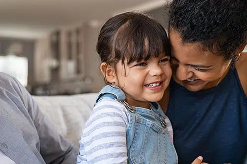 Smiling young girl in striped shirt and denim overalls cuddling with a man on a couch (family moment).