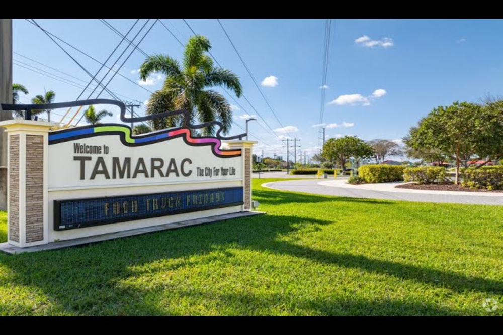 Tamarac - Akilah Harris, PLLC. Tamarac city welcome sign on a grassy area with palm trees and a digital message board about Food Truck Fridays