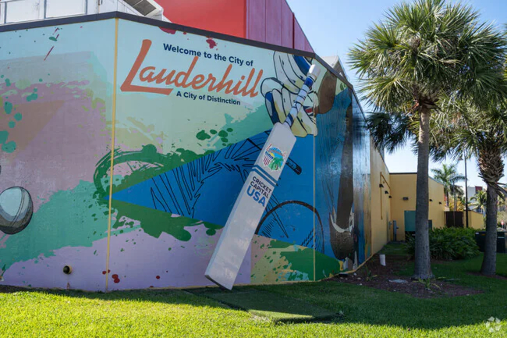 Colorful Lauderhill mural on a building with an oversized cricket bat leaning against the wall.
