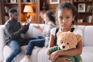Florida custody parent responsibility and time sharing laws - Akilah Harris, PLLC. - Akilah Harris, PLLC. Young girl with a teddy bear looks sad while her parents argue in the background on a sofa in a living room.
