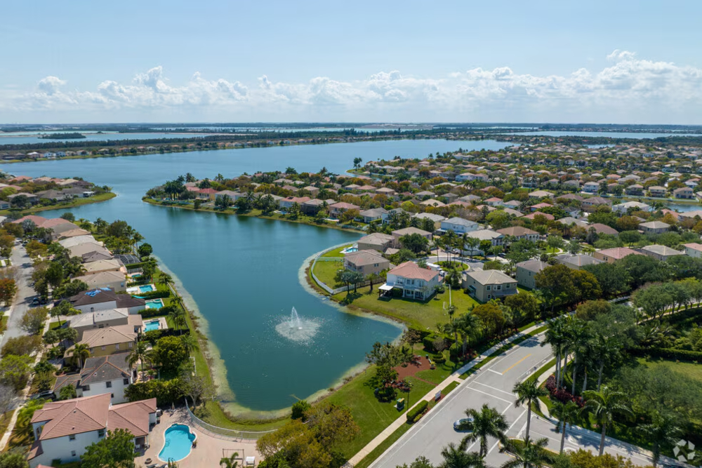 Aerial view of a suburban waterfront neighborhood with houses along a winding canal and a fountain in the water in the center.