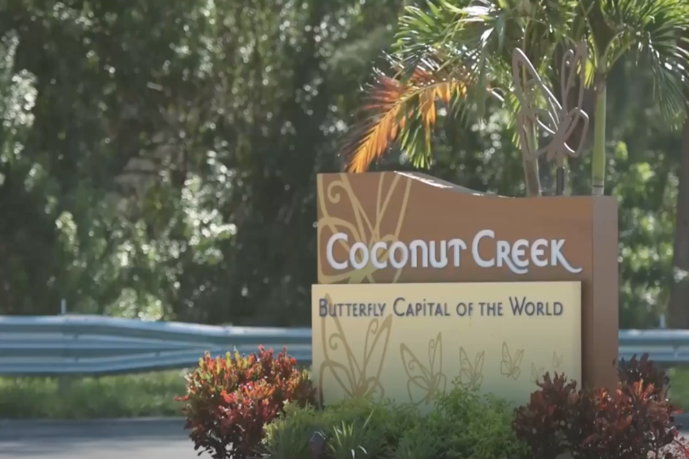 Coconut Creek - Akilah Harris, PLLC. Sign reading Coconut Creek: Butterfly Capital of the World, with tropical plant decorations nearby.
