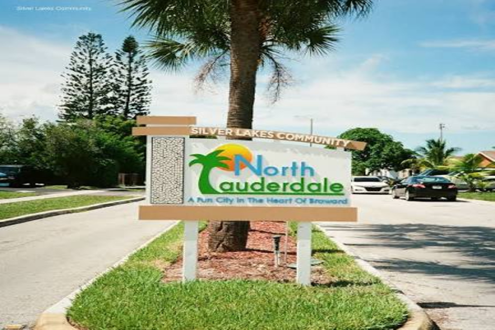 Sign for North Lauderdale city with palm tree graphic and slogan 'A Fun City In The Heart Of Broward' on a landscaped median in a suburban street.